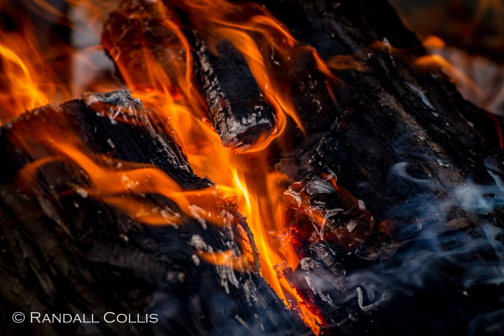 Close-up of burning logs with vibrant flames and smoke rising, creating a warm and dynamic atmosphere.