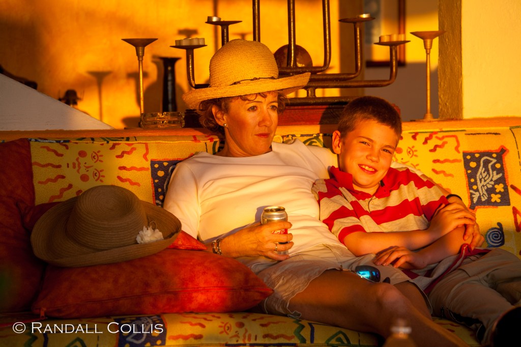 A woman and a boy sitting closely together on a couch, enjoying each other's company during a warm sunset, with soft lighting enhancing their relaxed expressions.